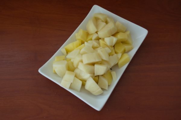 Нарезанный кубиками сырой картофель на прямоугольной белой тарелке