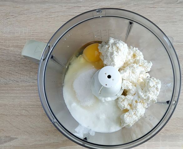 Творог, сырое яйцо, натуральный йогурт и сахар в чаше стационарного блендера