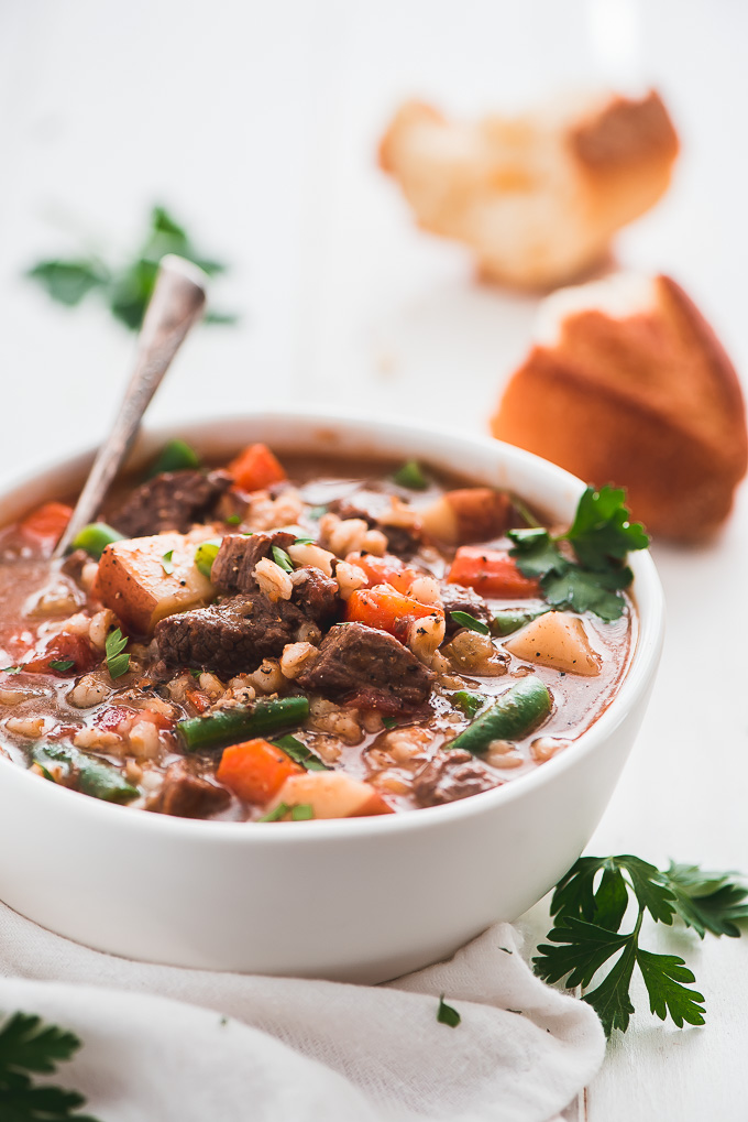 A bowl of Instant Pot Beef and Barley Soup garnished with black pepper and fresh parsley.
